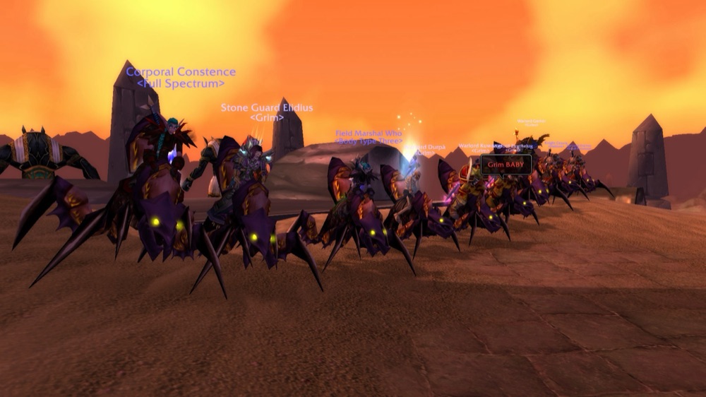 A line of Grim members on Black Qiraji Battle Tanks in Silithus at sunset, guild tags and vanilla PvP ranks above their heads.